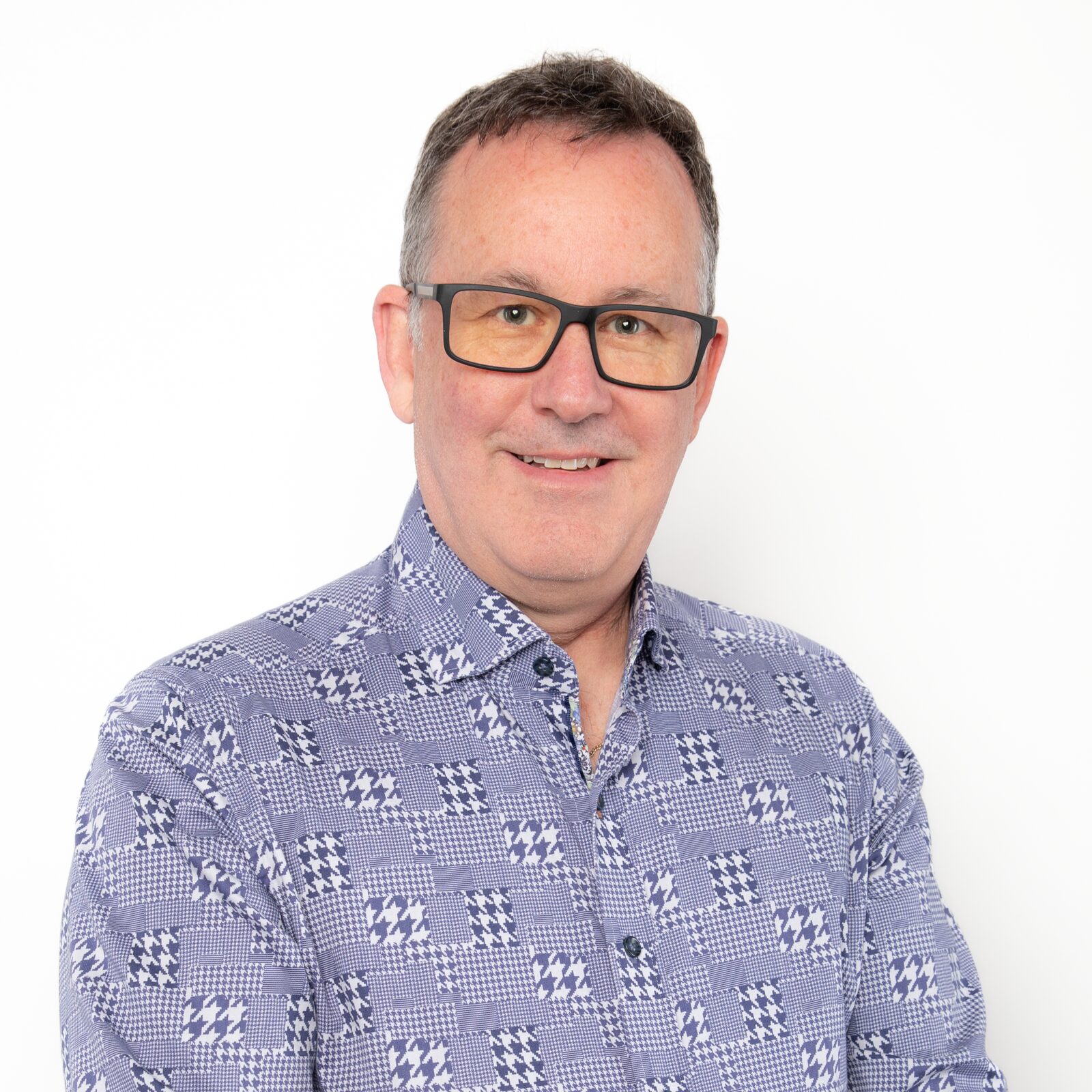 Kevin O. Larkin, smiling, in glasses and a patterned blue shirt